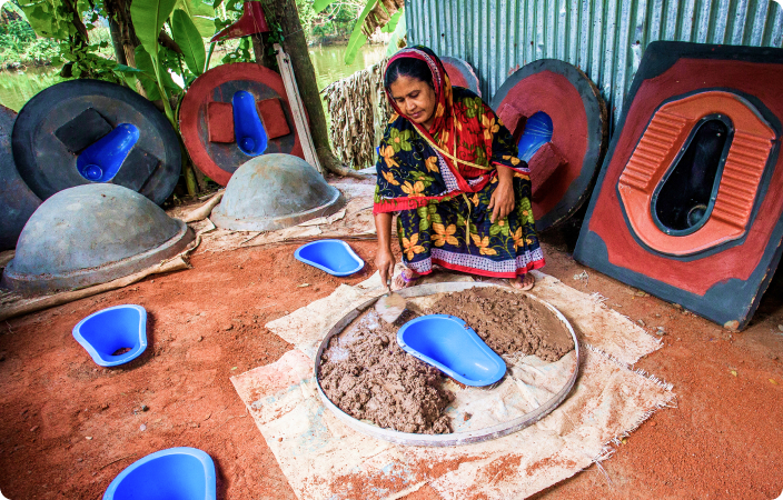 A women is making toilet seats in a rural area using clay and mud.